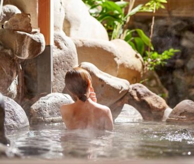 Person bathing in rock-lined indoor onsen with garden view at AKARI et KAORI Shizuoka