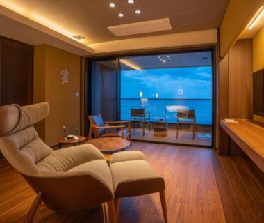 Recliner and wooden interior opening to balcony with sea view at AMANE resort GAHAMA in Okinawa