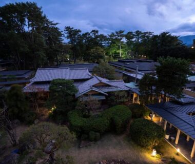 Elevated dusk view of tiled roofs, garden and lit pathways at AMANE resort GAHAMA in Ōita, Kyūshū