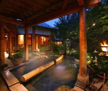 Steaming outdoor onsen bath with wooden beams and lanterns at Aishinkan, Iwate, Tōhoku
