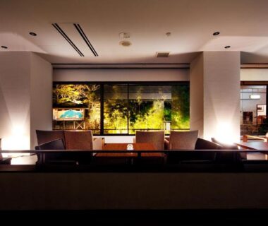 Dimly lit lounge with seating and illuminated garden view through large window at Aizu Higashiyama Onsen