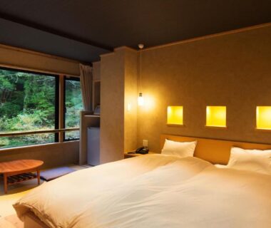 Tatami room with low table, Western bed and large window overlooking forest at Aizu Higashiyama Onsen Fukushima