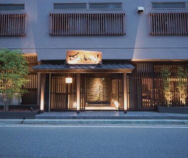 Lit wooden entrance with noren at Aizu Higashiyama Onsen Tsuki no Akari, street-level facade in Fukushima