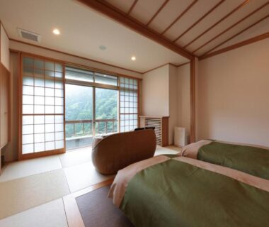 Tatami room with twin beds, shoji screens and balcony overlooking forested hills at Akagi Onsen Hotel Gunma
