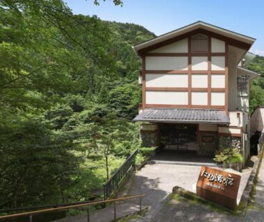 Traditional multi-story ryokan building entrance beside lush forested hillside in Gunma prefecture