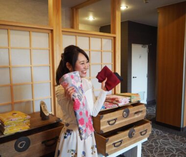 Guest holding folded yukata in corridor with shoji screens and wooden chests