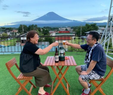 Two guests clinking glasses at rooftop table with bottles and mountain backdrop at Akaishi Ryokan, Yamanashi