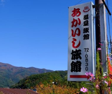 Vertical sign for Akaishi Ryokan beside roadside flowers with mountains in the background, Yamanashi Chūbu