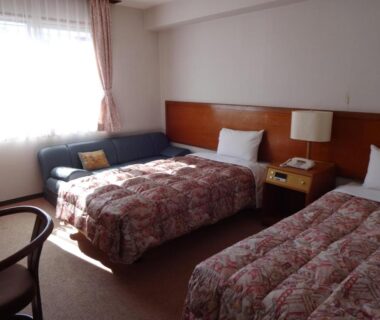 Twin beds with patterned bedspreads, sofa and bedside lamp at Akakura Hotel in Niigata