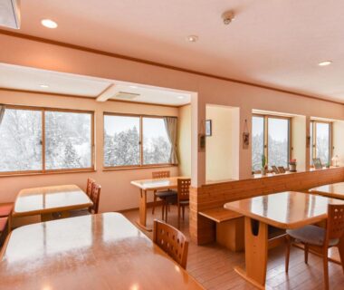 Bright dining area with wooden tables, bench seating and large windows at Akakura onsen eho ryokan Niigata