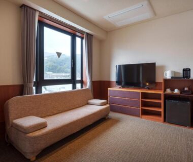 Sofa, television, and large window with hillside view in Akarinoyado Togetsu guest room, Ōita