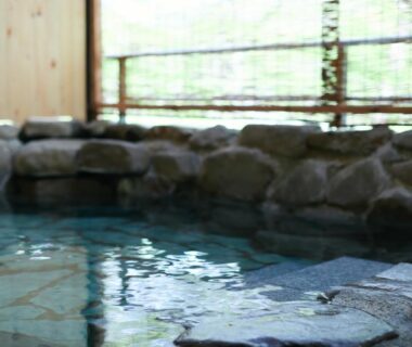 Indoor stone onsen bath with rock edging and wooden lattice window at Akiu Fuga, Miyagi