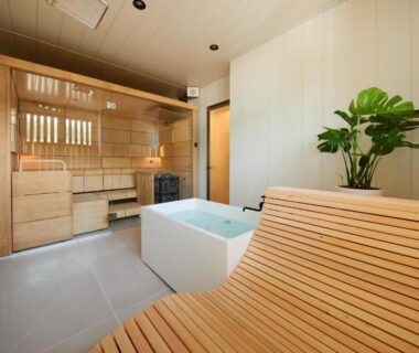 Wooden-lined indoor onsen room with soaking tub, curved wooden lounge bench and shower at Akiu Fuga, Miyagi
