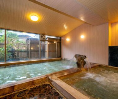 Indoor tiled onsen baths with wooden spout and garden view at Ama no Shima Mie