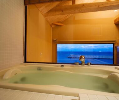 Indoor soaking tub with ocean view through wide window and wooden beam ceiling at Amahara, Hyōgo