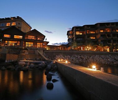 Nighttime waterfront ryokan buildings reflecting in river with lantern-lit walkway, Amahara, Hyōgo, Kansai