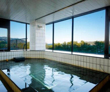 Tiled indoor onsen bath with large windows overlooking treetops and water at Amanohashidateso in Kyoto, Kansai