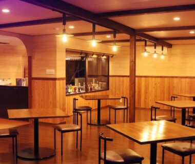 Warm wood-paneled dining area with small bar counter, square tables and stools at Amis Droles in Shizuoka
