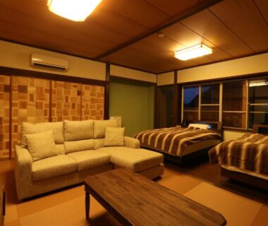 Tatami room with sofa, low table and two beds at Amis Droles in Shizuoka