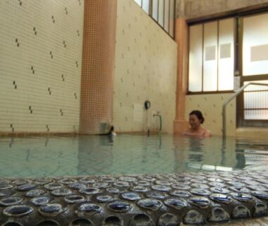 Guest soaking in tiled indoor onsen bath with low mosaic edge and wooden screen windows