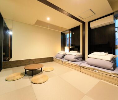 Minimal tatami room with low table, floor cushions and stacked futons near window at Andon Ryokan Tokyo