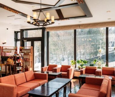 Bright lounge with orange sofas, low tables and bookshelf at Appikogen Mori no Hotel in Iwate, Tōhoku