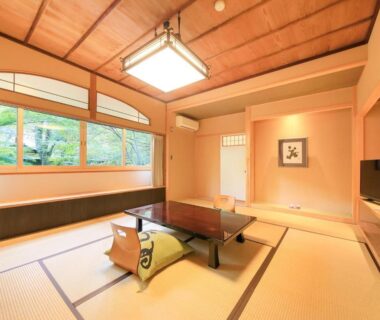 Tatami room with low table, cushions, wood-framed windows and decorative alcove at Arai Ryokan, Shizuoka