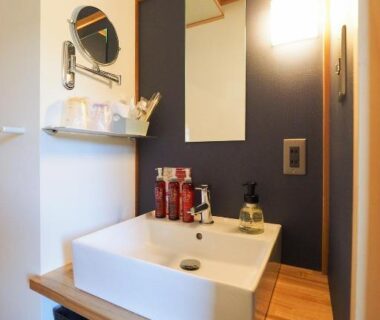 Compact vanity with white rectangular basin, wooden counter, mirror and toiletries at Arai Ryokan, Shizuoka