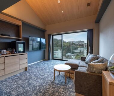 Relaxing lounge area with sofa, coffee table, TV and large window overlooking Arima Onsen town in Hyōgo