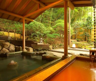 Outdoor hot spring baths with wooden roof, stone surrounds and garden setting at Arima Onsen Taketoritei Maruyama, Hyōgo