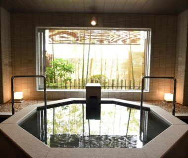Octagonal indoor bathing pool with central spout, timber accents and bamboo screen window overlooking a small garden at Arima Onsen