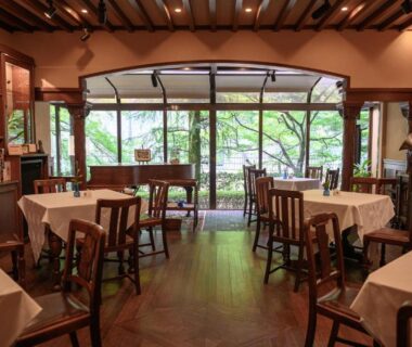 Wood-floored ryokan dining area with white tablecloths, wooden chairs and garden view through large windows