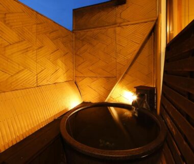 Outdoor round wooden bath on terrace with warm lighting and wooden screens at Arima Royal Hotel, Hyōgo