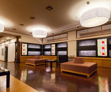 Spacious ryokan lounge with wooden floors, low benches and pendant lights at Arimakan in Yamagata