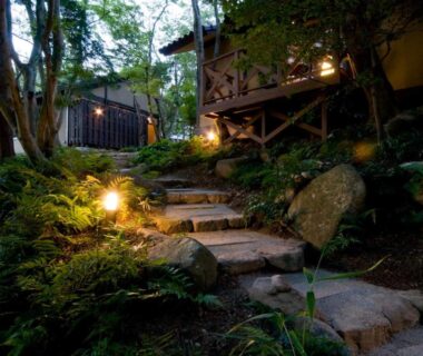 Lantern-lit mossy stone steps leading to a raised wooden ryokan building in a forested hillside, Arimasansoh Goshobessho, Hyōgo