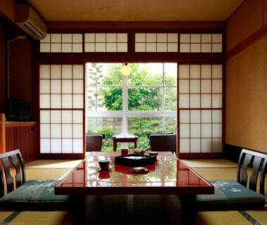 Traditional tatami room with low lacquered table, zabuton cushions, shoji screens and leafy garden visible through sliding doors