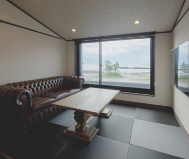 Tatami seating area with low wooden table, leather sofa, and large window overlooking water at Arujisu, Chūbu, Japan