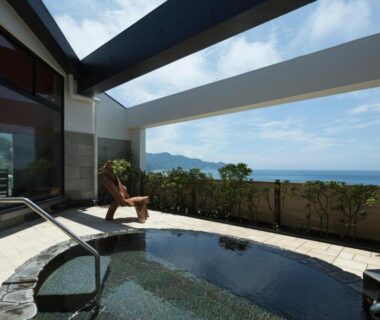 Stone-lined outdoor onsen bath with ocean view and glass roof at Arujisu ryokan in Shizuoka