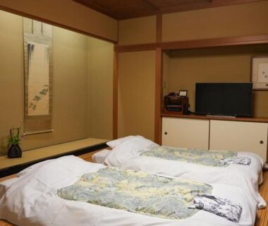 Traditional tatami room with futon bedding, tokonoma alcove with hanging scroll and vase at Asadaya, Ishikawa