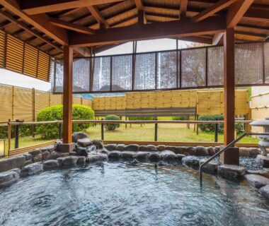 Covered stone onsen bath with timber roof, surrounding rocks and a small enclosed garden at Asagiriso, Hyōgo