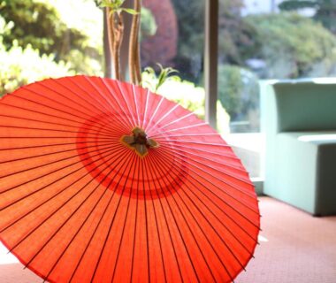 Red paper umbrella beside low seating with garden view at Asahikan in Nagano