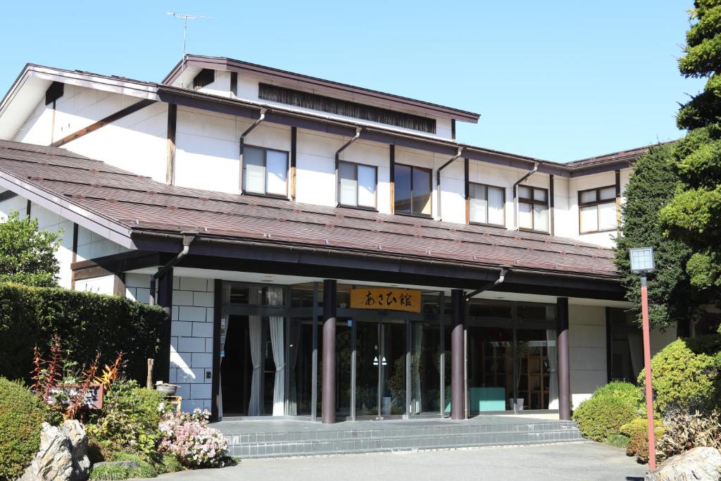 Entrance of Asahikan in Nagano Two story ryokan facade with tiled roof, glass doors and manicured shrubs at Asahikan in Nagano Chubu