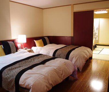 Twin beds with bedside lamp and cushions, adjacent tatami room visible at Asanoya in Hyōgo