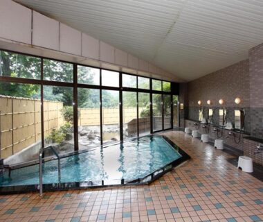 Shared indoor onsen with tiled floor, washing stations, stools and large windows overlooking garden