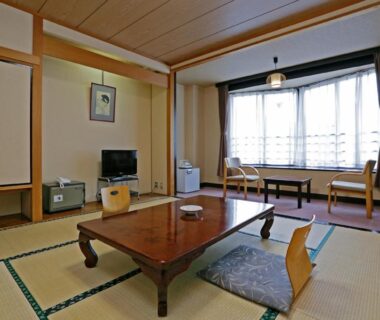 Traditional tatami room with low wooden table, floor cushions, window seating and shoji-style sliding doors at Ashinomaki Prince Hotel