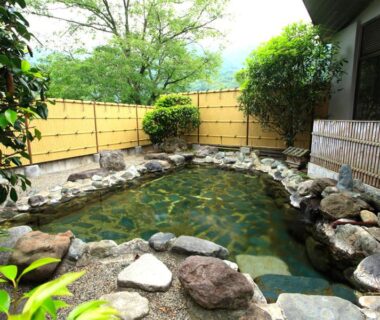 Rock-lined onsen bath with bamboo fence and garden greenery at Ashinomaki Prince Hotel, Fukushima