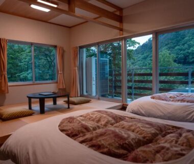 Tatami room with futon bedding, low table and floor cushions, sliding doors to wooded hillside balcony