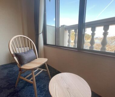 Wooden chair and round table by window with balcony railing at Ashiwada Hotel in Yamanashi