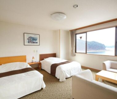 Two single beds and seating area facing lake through large window at Ashiwada Hotel, Yamanashi