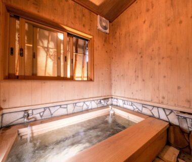 Wooden indoor soaking tub with stone trim and shoji window at AsoTsuruya, Kumamoto, Kyushu, Japan